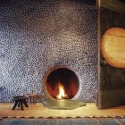 river rock covered fireplace wall with circular firebox opening - fine home building via atticmag